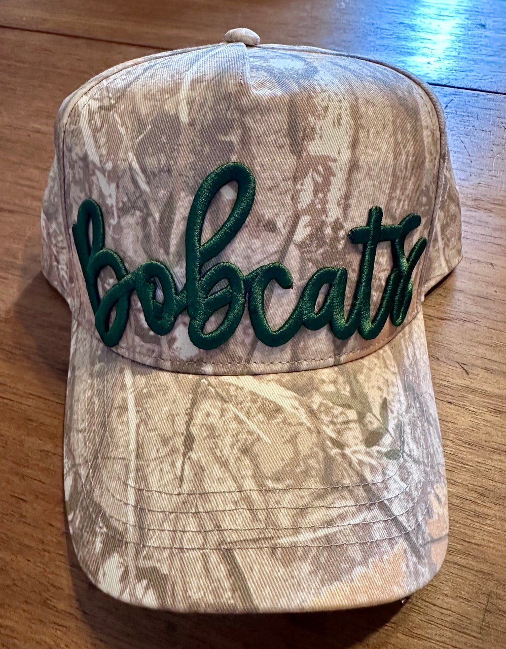 Close-up of Greenbrier Bobcats puff embroidered camo hat in forest green on all-camo base