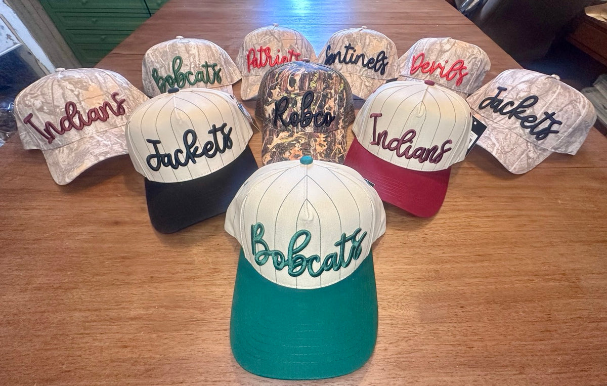 Puff embroidered mascot patch hats in pinstripe camo with colored brims — Indians, Jackets, Bobcats, Patriots, Sentinels, Devils displayed with RobCo camo trucker hat